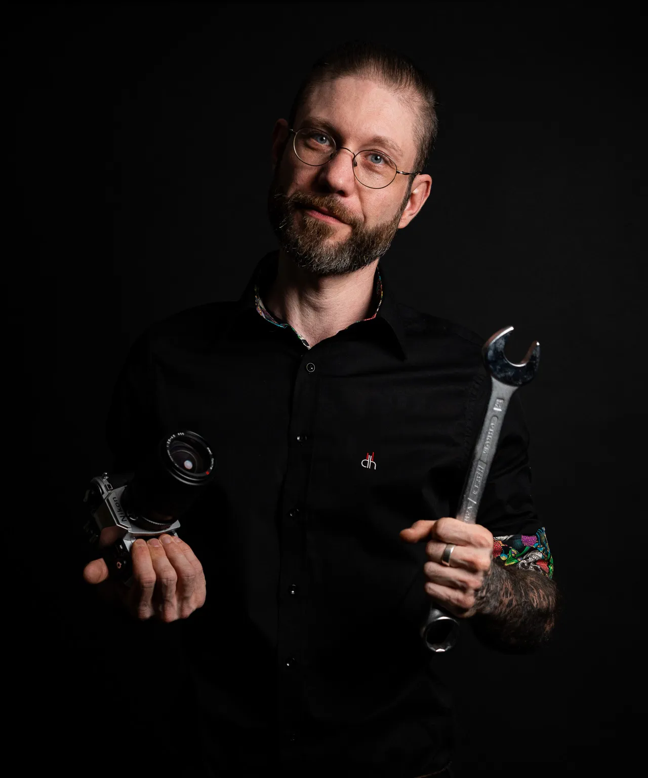 Portrait eines Fotografen mit Kamera und Werkzeugschlüssel in der Hand; Symbolbild für die Kombination aus handwerklicher Präzision und visueller Kommunikation in Stuttgart.